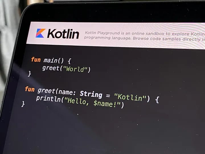 Screenshot of Kotlin Playground showing a simple program with functions `main` and `greet` to print greetings in the Kotlin programming language.